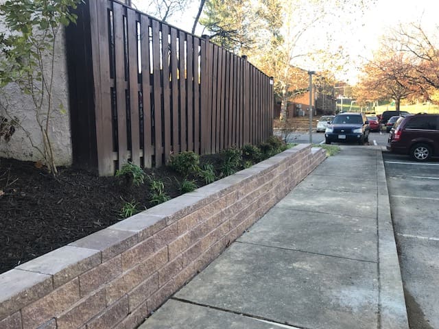 A sidewalk with a brick wall and wooden fence.